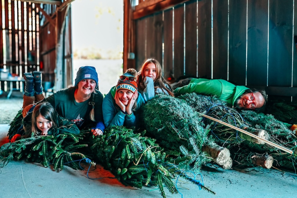 Members of the Hutton-Loyd family laying on a pile of Christmas trees.